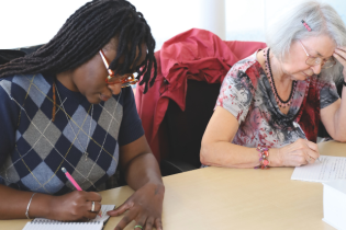Deux personnes adultes penchées sur une table en train d'écrire.