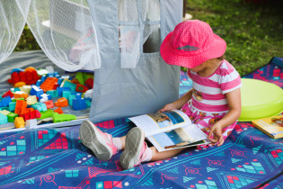 Petite fille lisant un livre à l'espace mini-biblio d'une Fête de quartier.