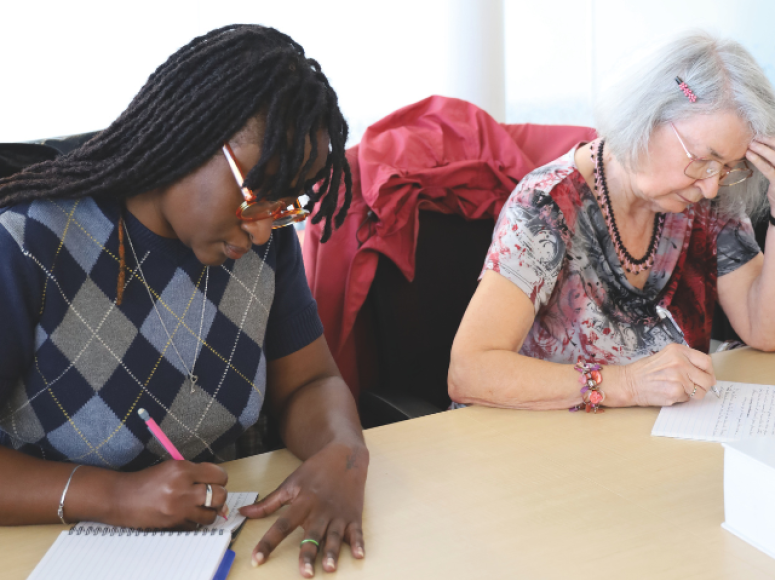 Deux personnes adultes penchées sur une table en train d'écrire.