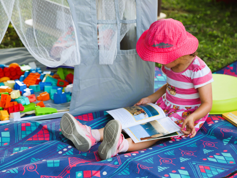 Petite fille lisant un livre à l'espace mini-biblio d'une Fête de quartier.