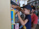 Jeune enfant sélectionnant un livre dans les étagères de la bibliothèque. Son père est accroupi juste derrière lui.