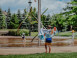 Enfant de dos avec une serviette près des jeux d'eau.